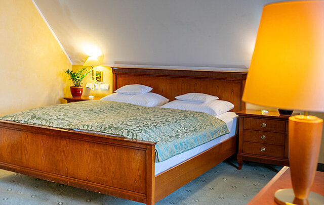 [Translate to English:] Doppelbett mit grünem Bezug und Lampe